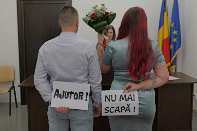 A man and a woman holding signs reading AJUTOR and NU MAI SCAPĂ