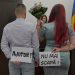 A man and a woman holding signs reading AJUTOR and NU MAI SCAPĂ