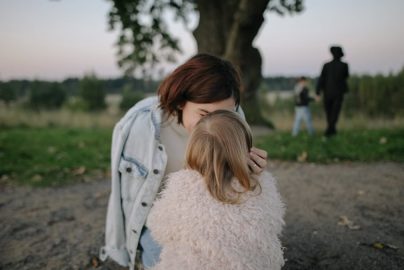 A tender moment between mother and daughter outdoors in a grassy field at twilight.